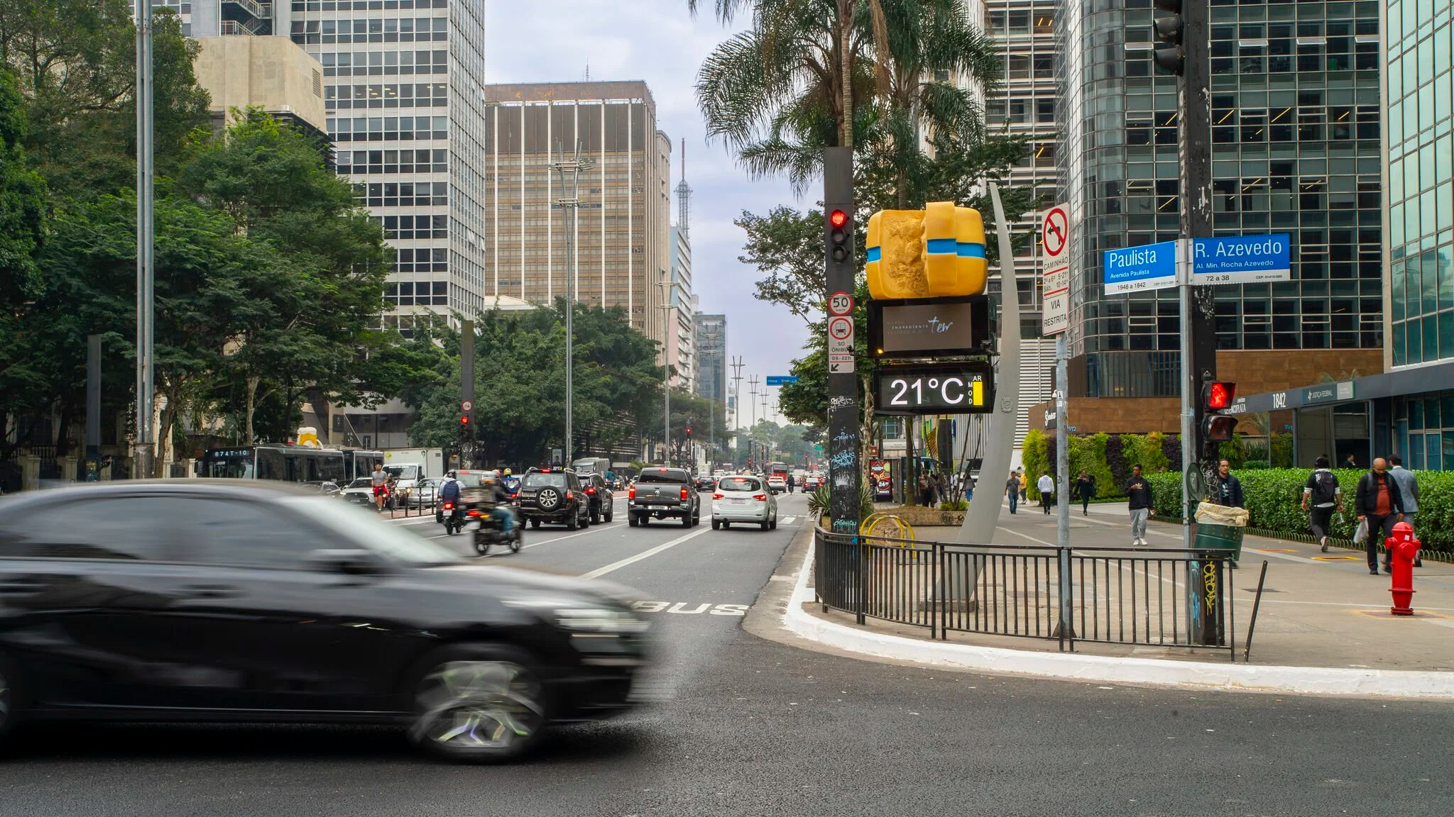 Faixa Azul giant cheese installation above a digital street clock on a busy São Paulo avenue.