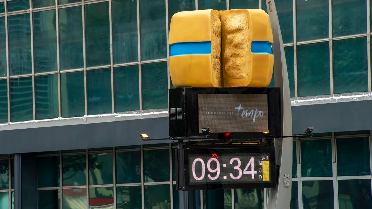 Faixa Azul outdoor installation with a giant cheese wheel above a street clock, promoting the campaign “Nosso ingrediente secreto é o tempo.”
