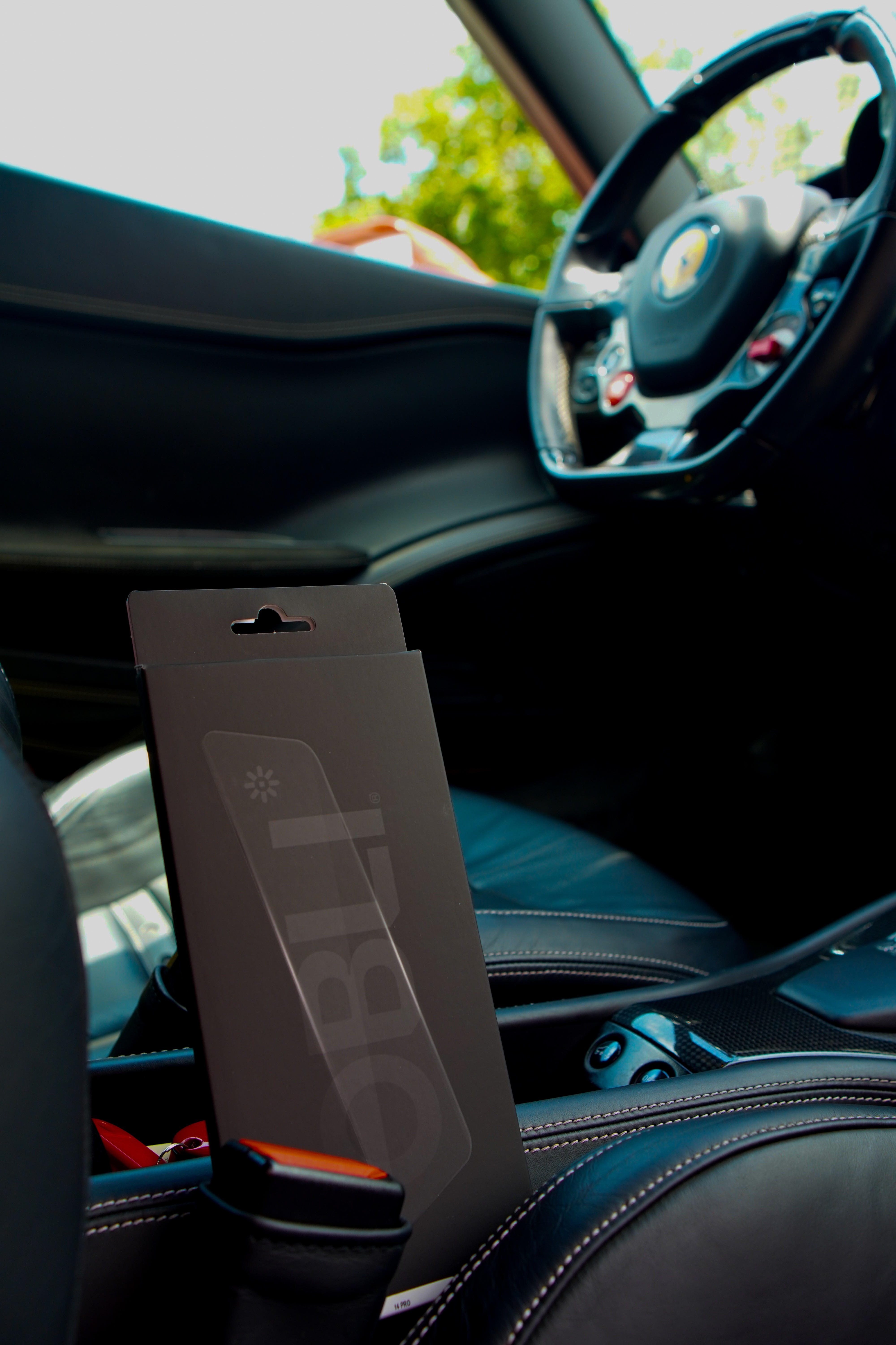 Obli smartphone accessory packaging photographed inside a car beside the steering wheel.