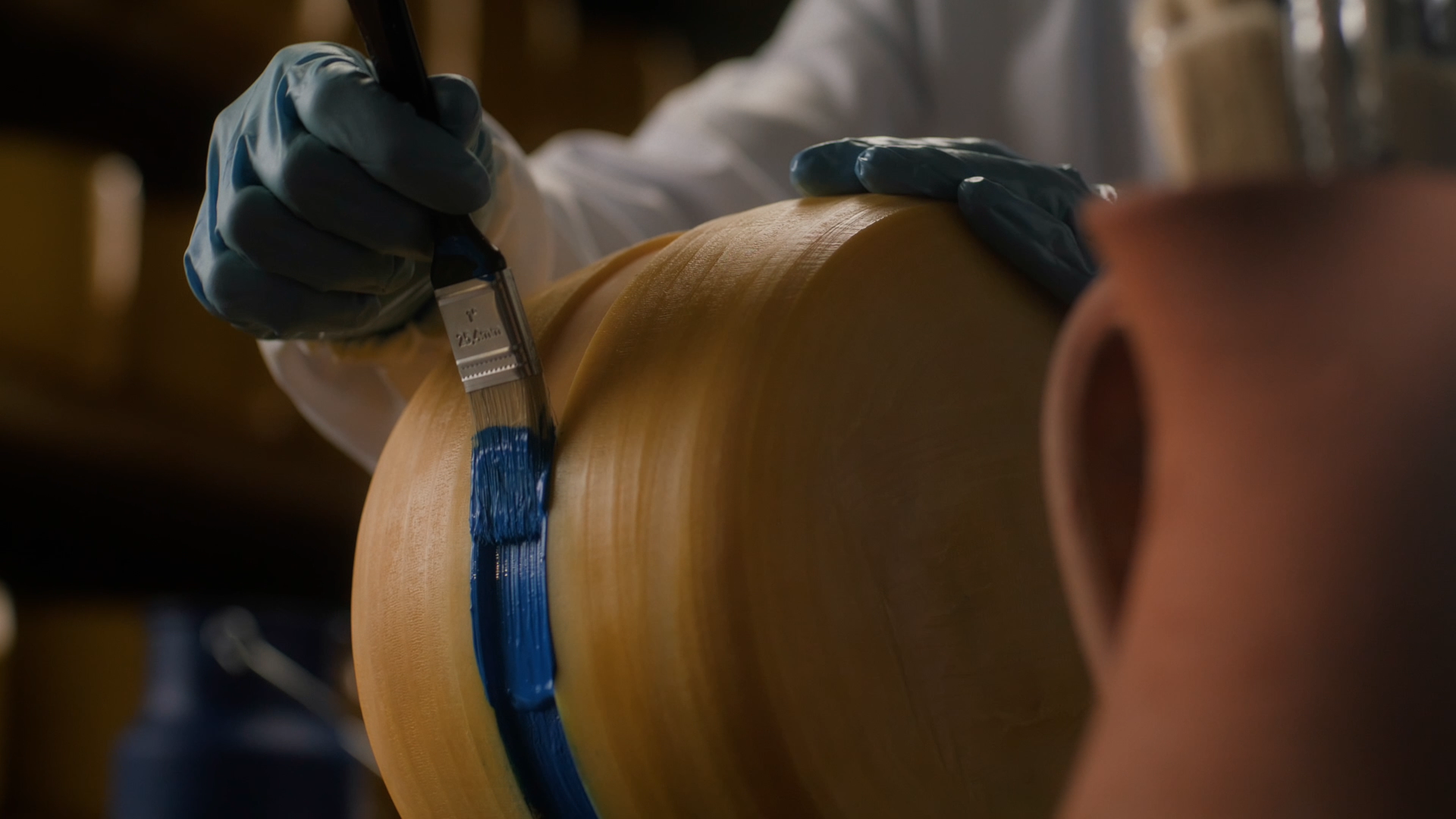 Faixa Azul cheese production close-up showing gloved hands securing the blue band around an aged cheese wheel.