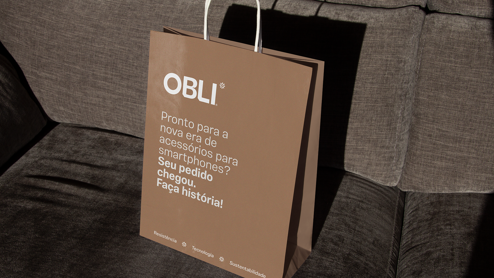 Obli kraft shopping bag with the white logo and smartphone accessories welcome message, resting on a sofa.