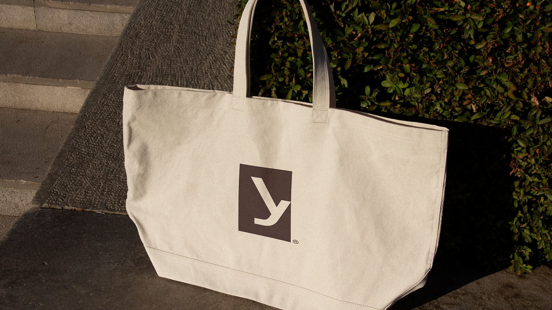 Yvi cream tote bag with a burgundy monogram, photographed on sunlit stone steps.