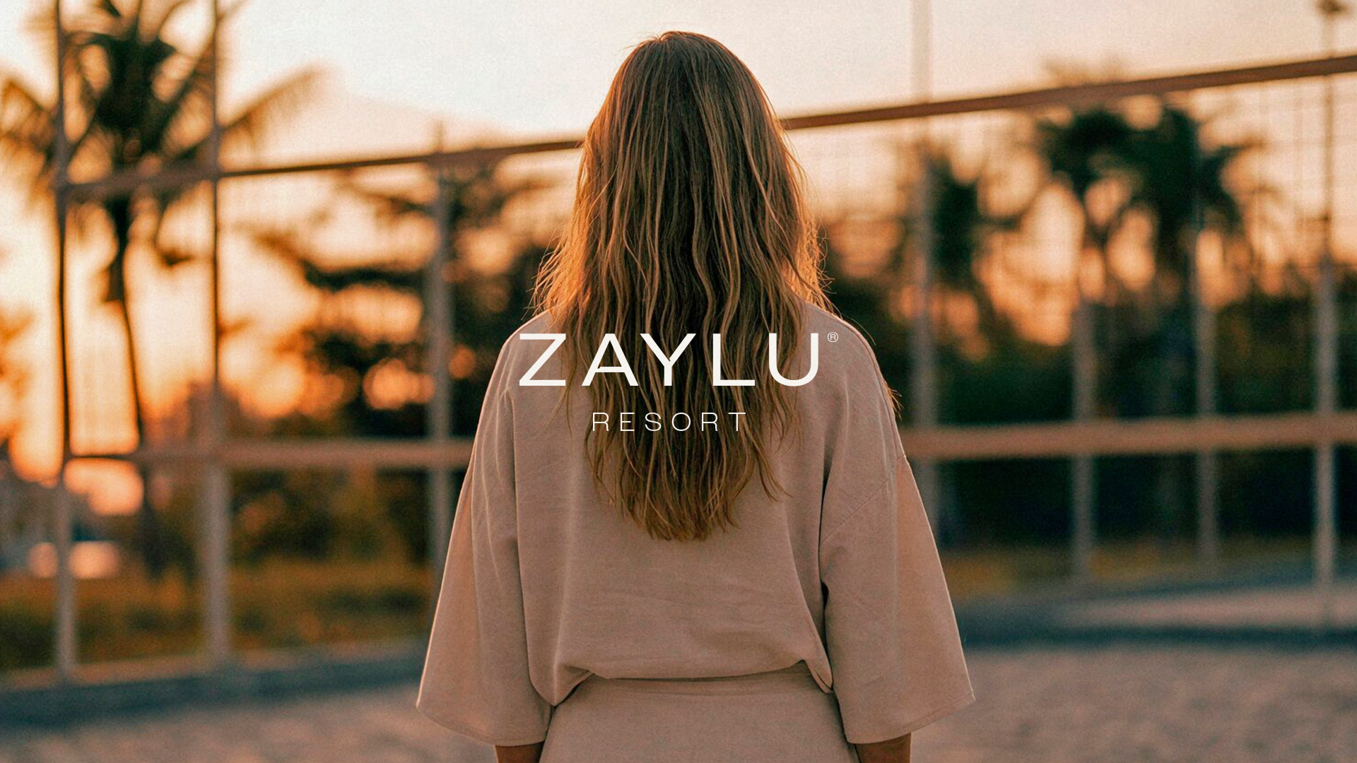 Zaylu Resort logo over a photograph of a woman facing the resort at sunset.