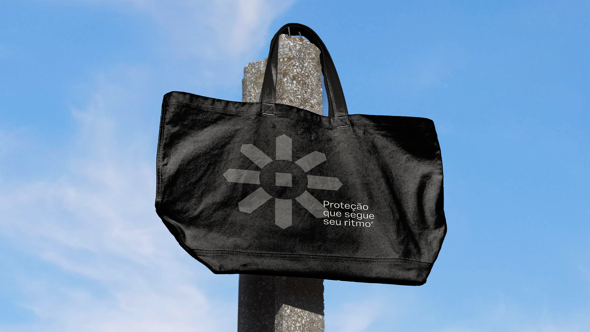 Obli black tote bag with the geometric brand symbol, photographed against a blue sky.