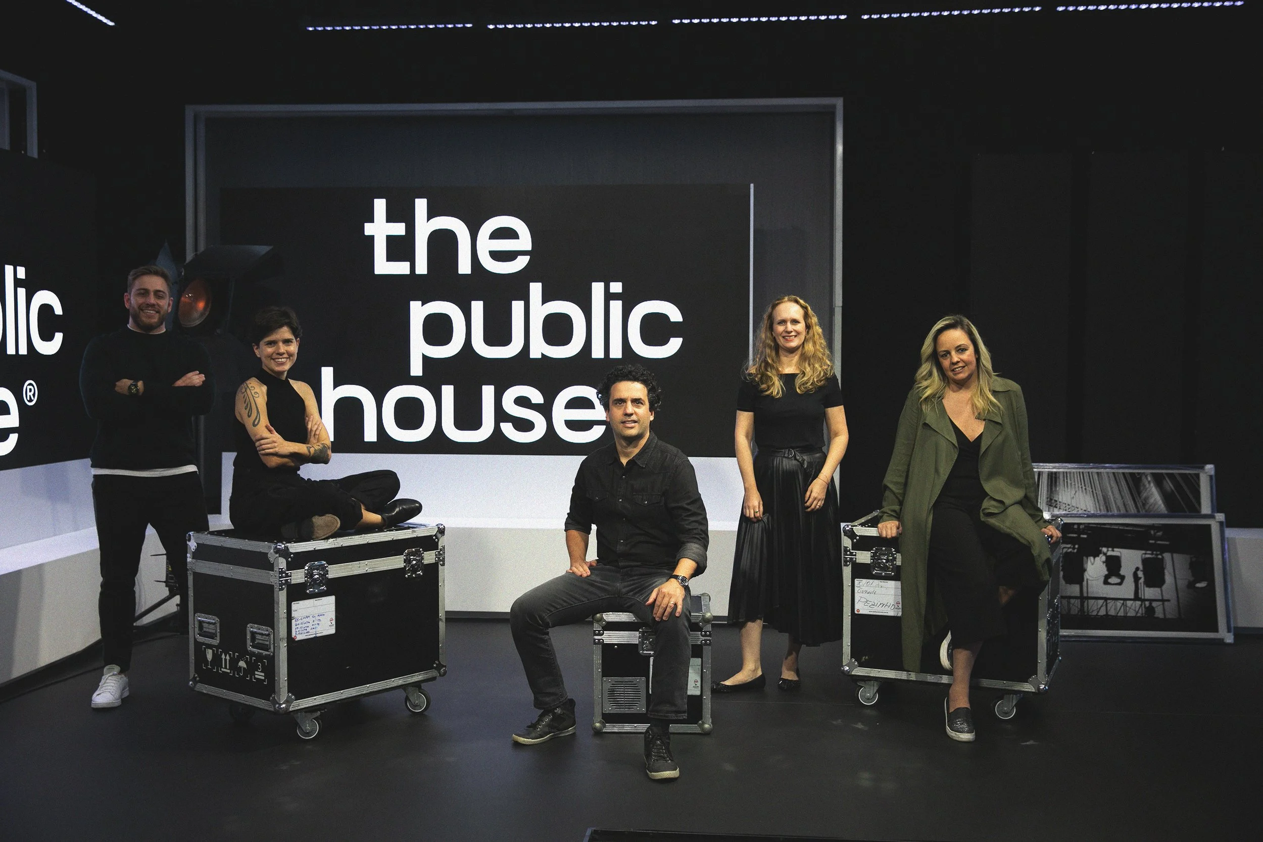 The Public House team photographed on the studio stage beside equipment cases and the illuminated wordmark.