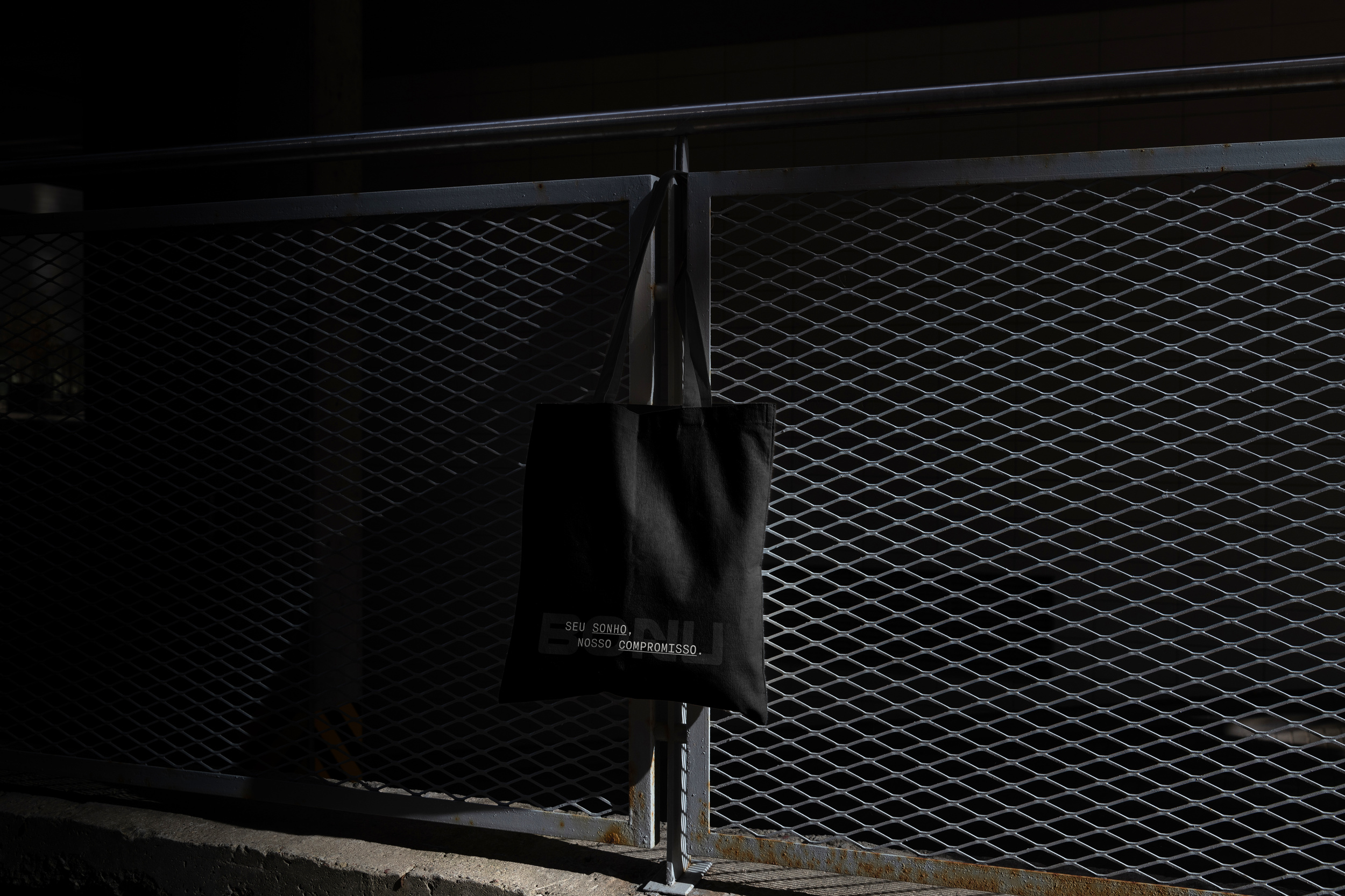 BONU black tote bag hanging on a metal fence with the message Seu sonho, nosso compromisso.